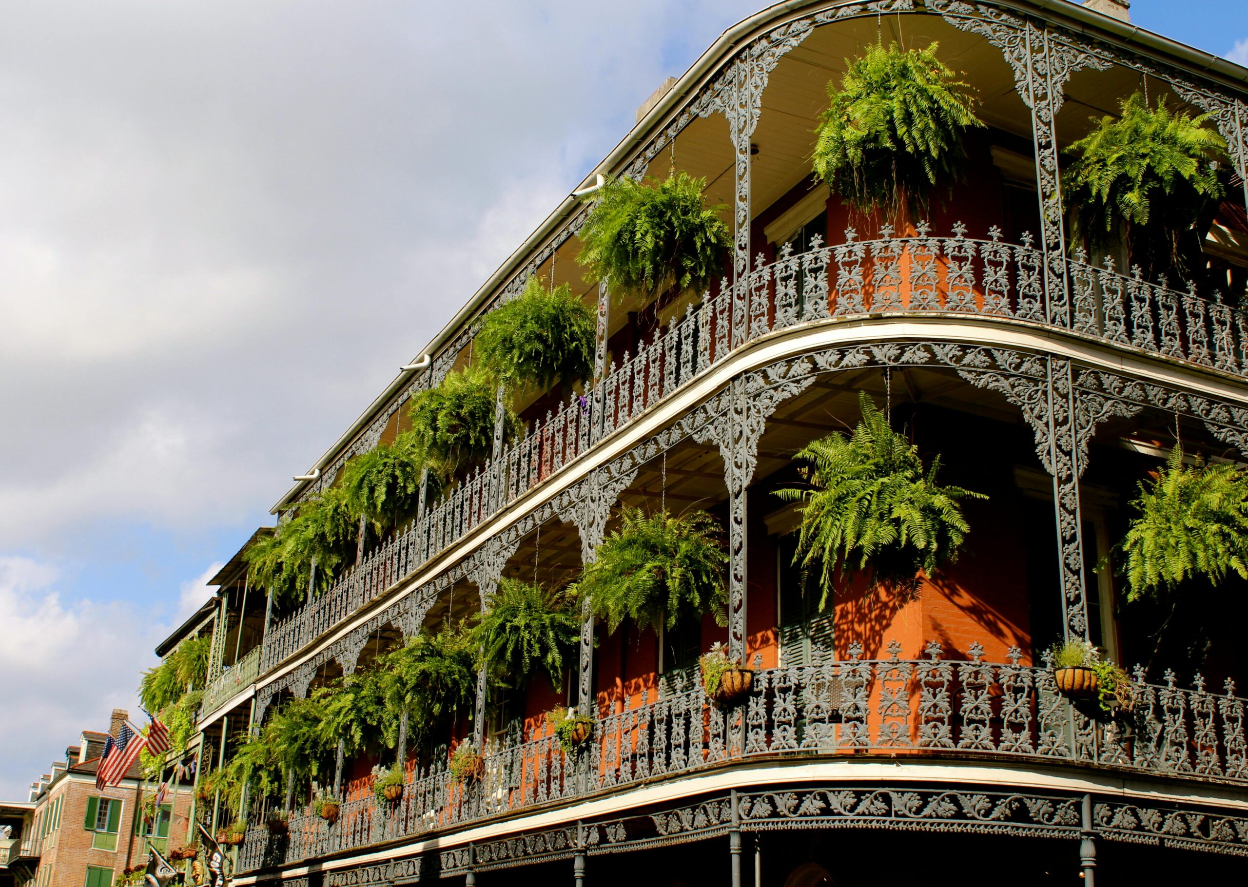 Detailed view of ornate ironwork balconies with lush greenery in New Orleans under a vibrant sky.