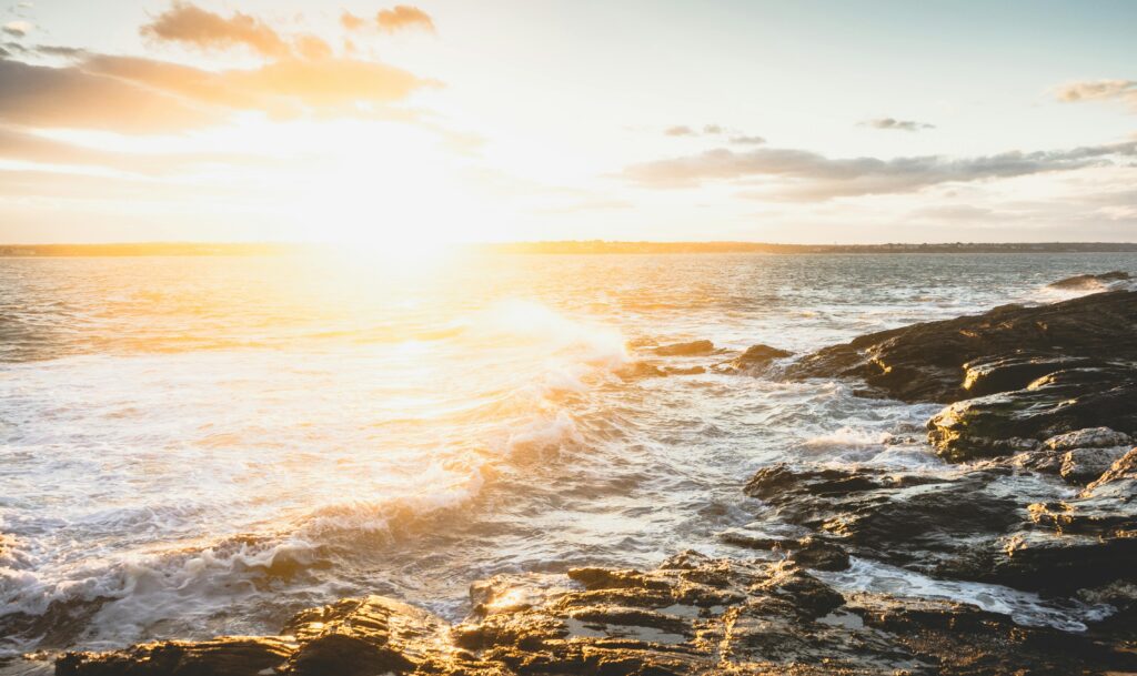Golden sunrise over the rocky coastline of Jamestown, RI, United States, casting warm hues on ocean waves.