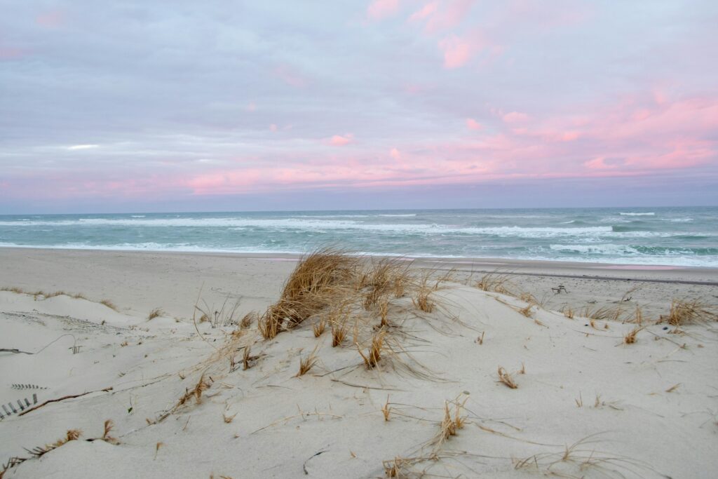 Peaceful sandy beach in Provincetown, MA with pink dawn sky and ocean waves.